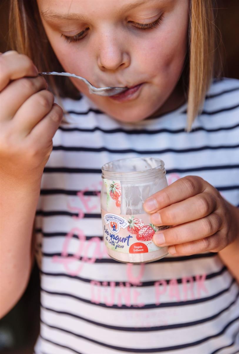 Kleines Mädchen isst Milchhof Sterzing Yogurt im Glas mit Löffel
