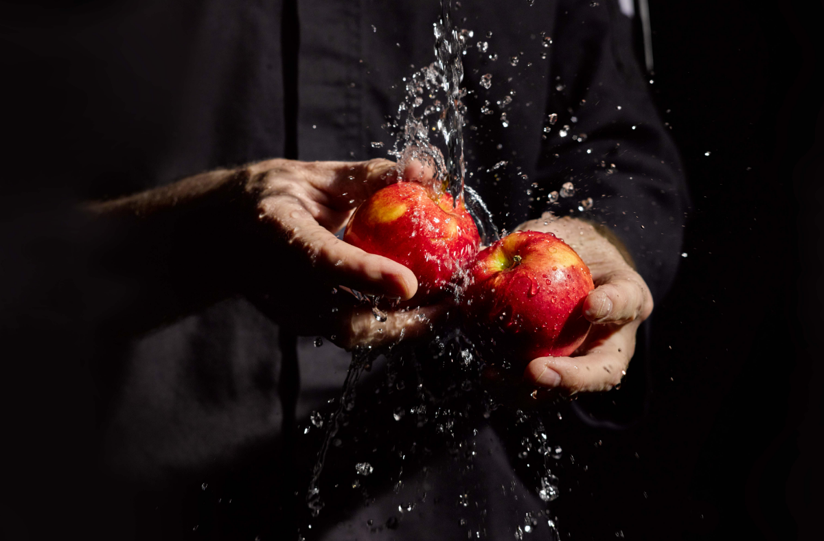 Koch hält zwei Äpfel in den Händen im Hintergrund spritzt Wasser drauf - Referenzbild Wedl Österreich